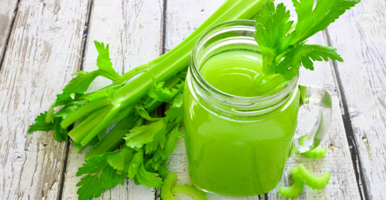 Celery juice in a mason jar glass. Downward view over a rustic white wood background.